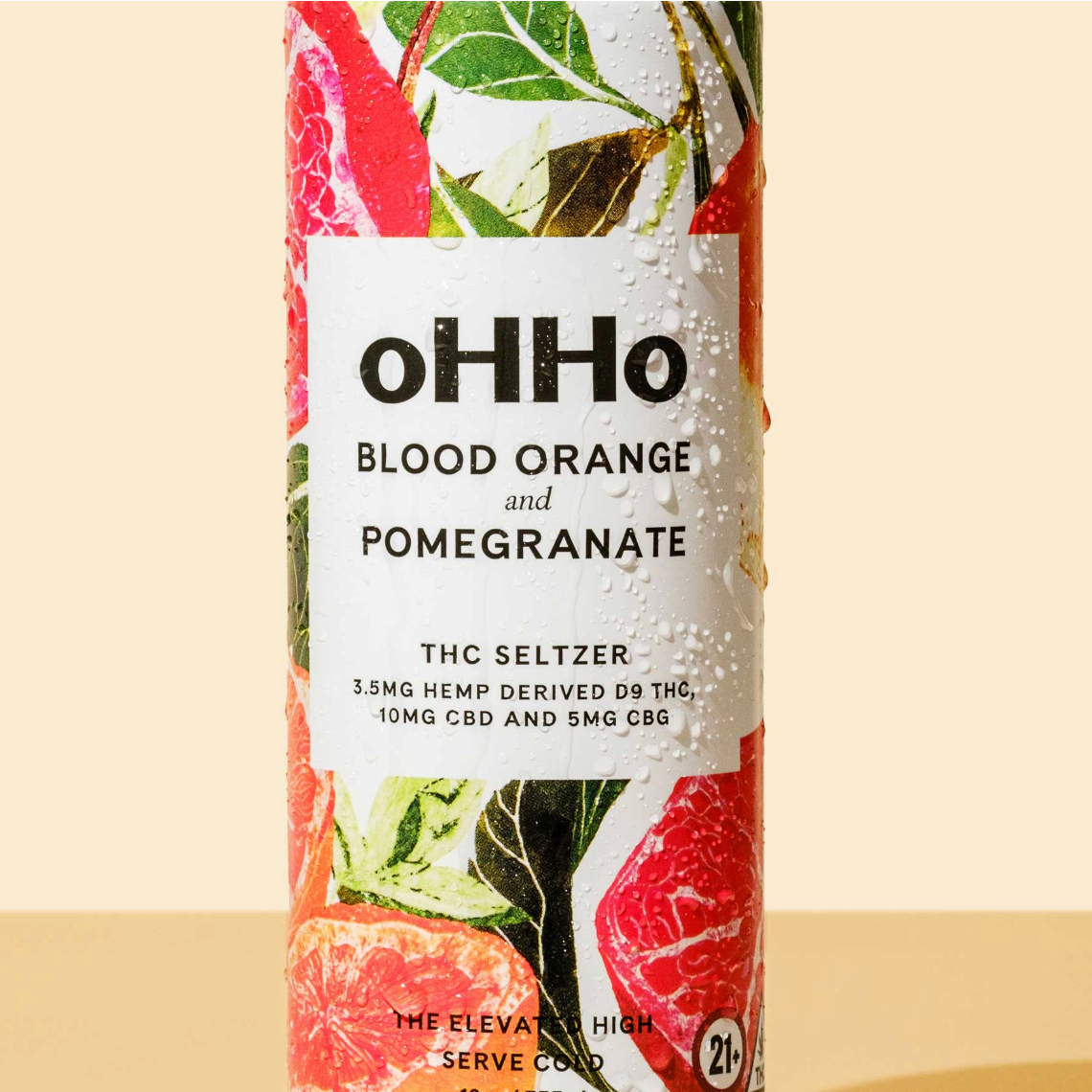 A cylindrical bottle of oHHo Blood Orange and Pomegranate THC Seltzer, featuring a white label with black text and a colorful background illustration of citrus slices and green leaves.