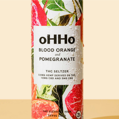 A cylindrical bottle of oHHo Blood Orange and Pomegranate THC Seltzer, featuring a white label with black text and a colorful background illustration of citrus slices and green leaves.