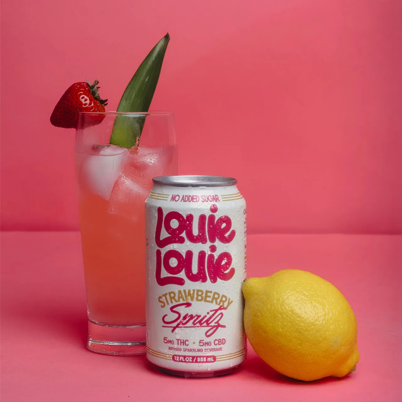 Louie Louie Strawberry Spritz can with a glass of strawberry lemonade and a lemon on a pink background